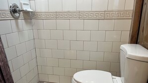 Et badeværelse med hvide fliser, toilet og bruseforhæng.