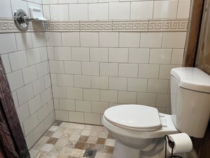 Une salle de bain avec des carreaux blancs, des toilettes et un rideau de douche.
