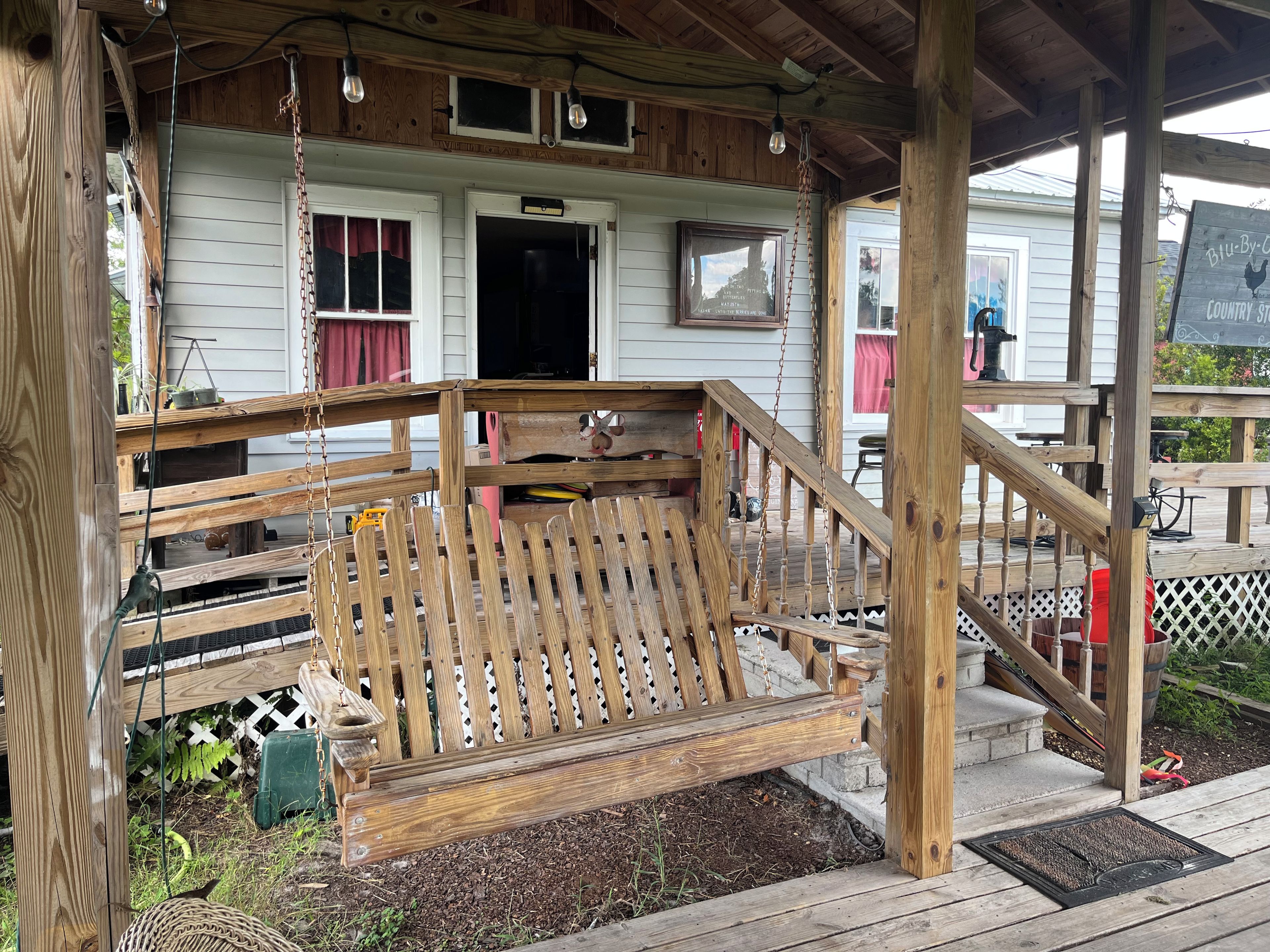 A wooden porch with a swing, a wooden staircase, and a house with a window and a door.