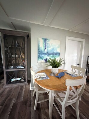 A dining area with a wooden table, white chairs, a potted plant, and a painting on the wall. - Cozy & Convenient 2-bedroom Cottage in Foley (Foley)