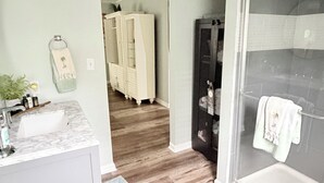 A bathroom with a shower, a sink, and a vanity. There is a hallway leading to a bedroom with a wardrobe. - Cozy & Convenient 2-bedroom Cottage in Foley (Foley)