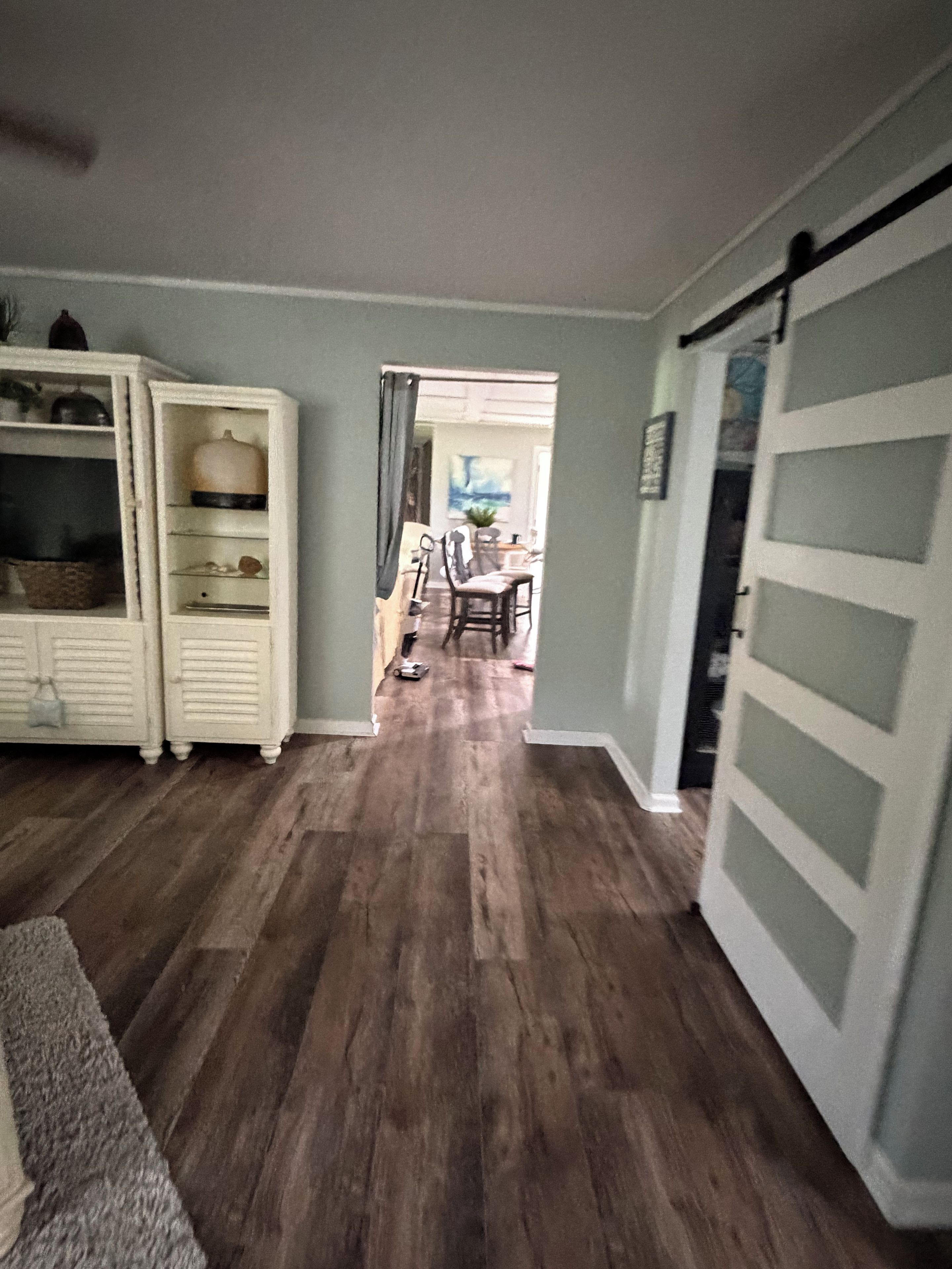 A hallway with a wooden floor leading to a dining area with a table and chairs.