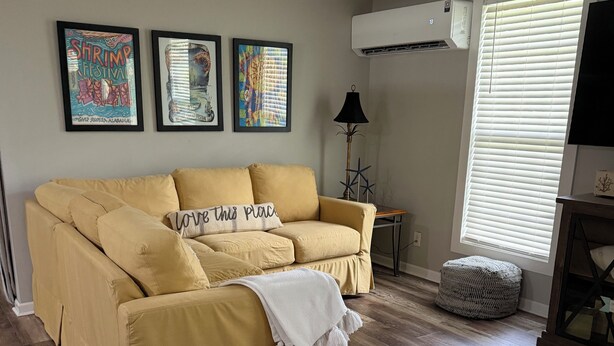 A living room with a yellow sofa, a white armchair, a ceiling fan, and a window with blinds. - Cozy & Convenient 2-bedroom Cottage in Foley (Foley)