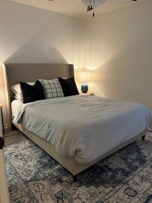 Ein ordentlich bezogenes Bett mit Kopfteil, einer Nachttischlampe und einem gemusterten Teppich.