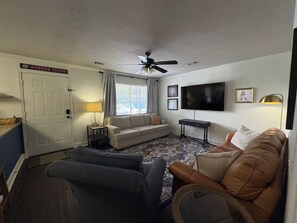 Ein Wohnzimmer mit einer Couch, einem Couchtisch, einem Fernseher und einem Deckenventilator.