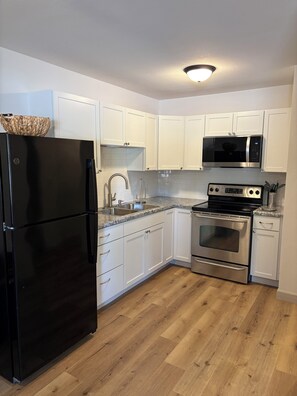 A kitchen with white cabinets, a black refrigerator, a microwave, and an oven. - Peaceful 1-bedroom apartment on large 2 acre lot. (Foster)