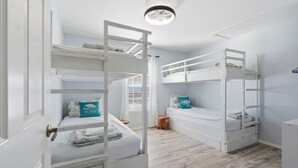 A room with bunk beds, a wooden stool, and a door with a brass handle. - Cape Cod Retreat 601-Pool & Playground-Sleeps 8 (Panama City Beach)