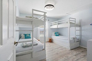 Quarto com beliches, um banquinho de madeira e uma porta com puxador de latão.