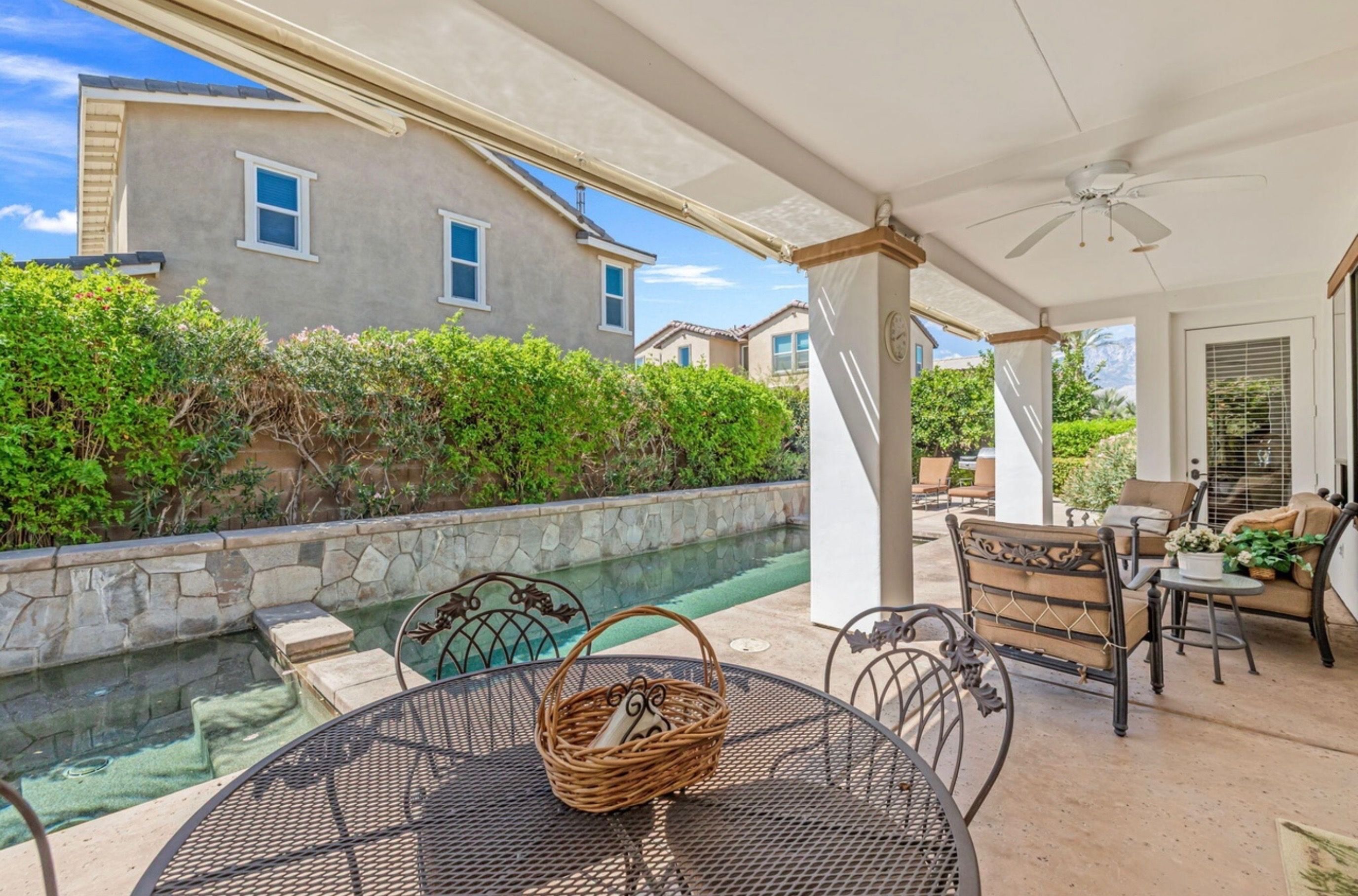 Un patio couvert avec une piscine, du mobilier d’extérieur et une vue sur une maison.