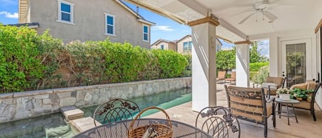 Un patio couvert avec une piscine, du mobilier d’extérieur et une vue sur une maison.