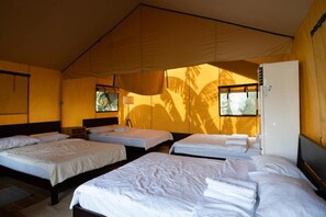 Ein Zimmer mit vier Betten, die in einer U-Form angeordnet sind, einem Kühlschrank und einem Fenster mit Blick auf Palmen.