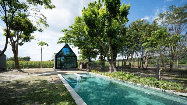 Una piscina con struttura in vetro, circondata da alberi e recinzione.