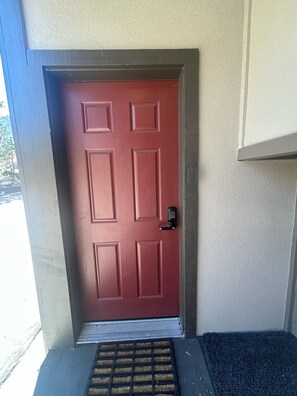 A red door with a keypad lock, a doormat, and a small step leading to the entrance.