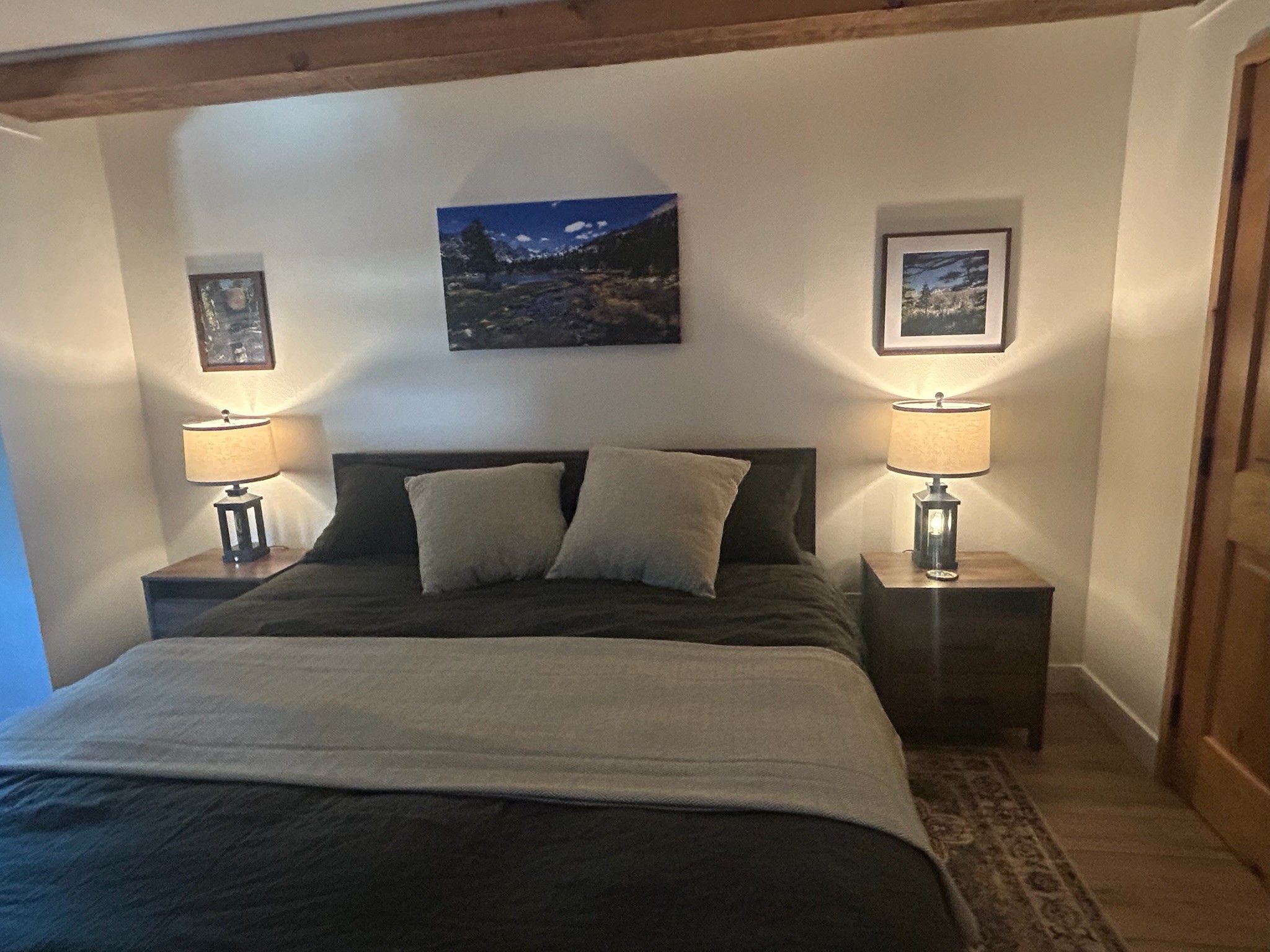 A bedroom with a bed, two nightstands, two wall-mounted lamps, and two framed pictures.
