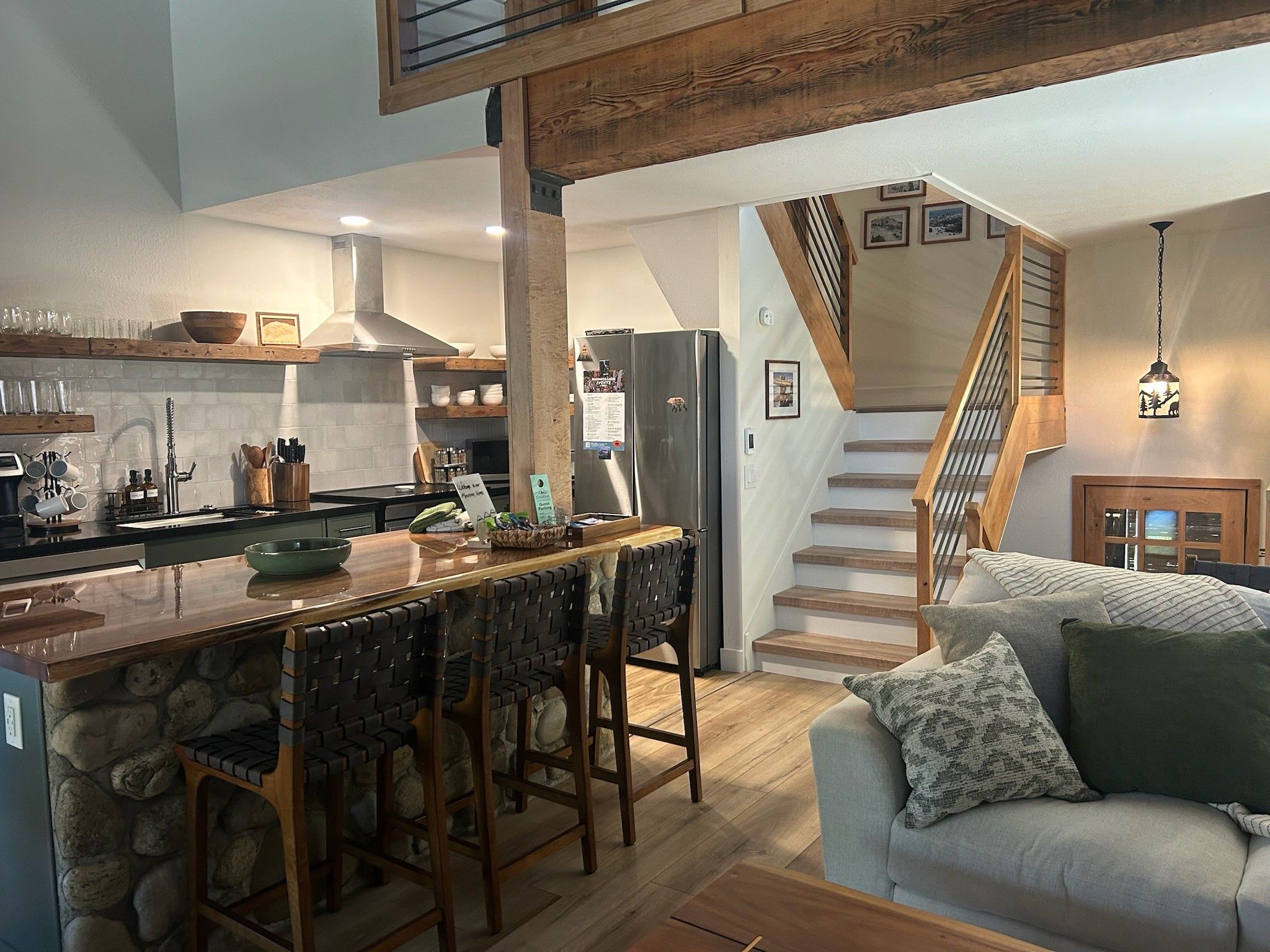 Een moderne keuken met een centraal eiland, houten barkrukken en een accentmuur van steen.