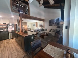 A modern kitchen with a central island, a dining area with a sofa and coffee table, and a living room with a couch and a painting.