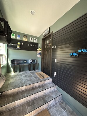 A garage with a skateboard, a surfboard, and a bicycle. There are shelves with helmets and a door with a sign.