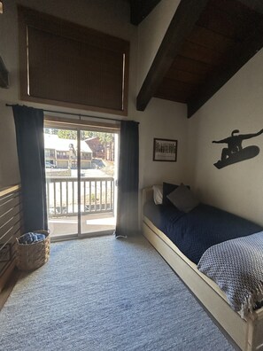 A room with a bed, a window with curtains, a wall-mounted picture, and a view of the outside.