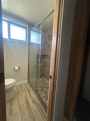Et badeværelse med glasbrusekabine, toilet og et vindue over toilettet.
