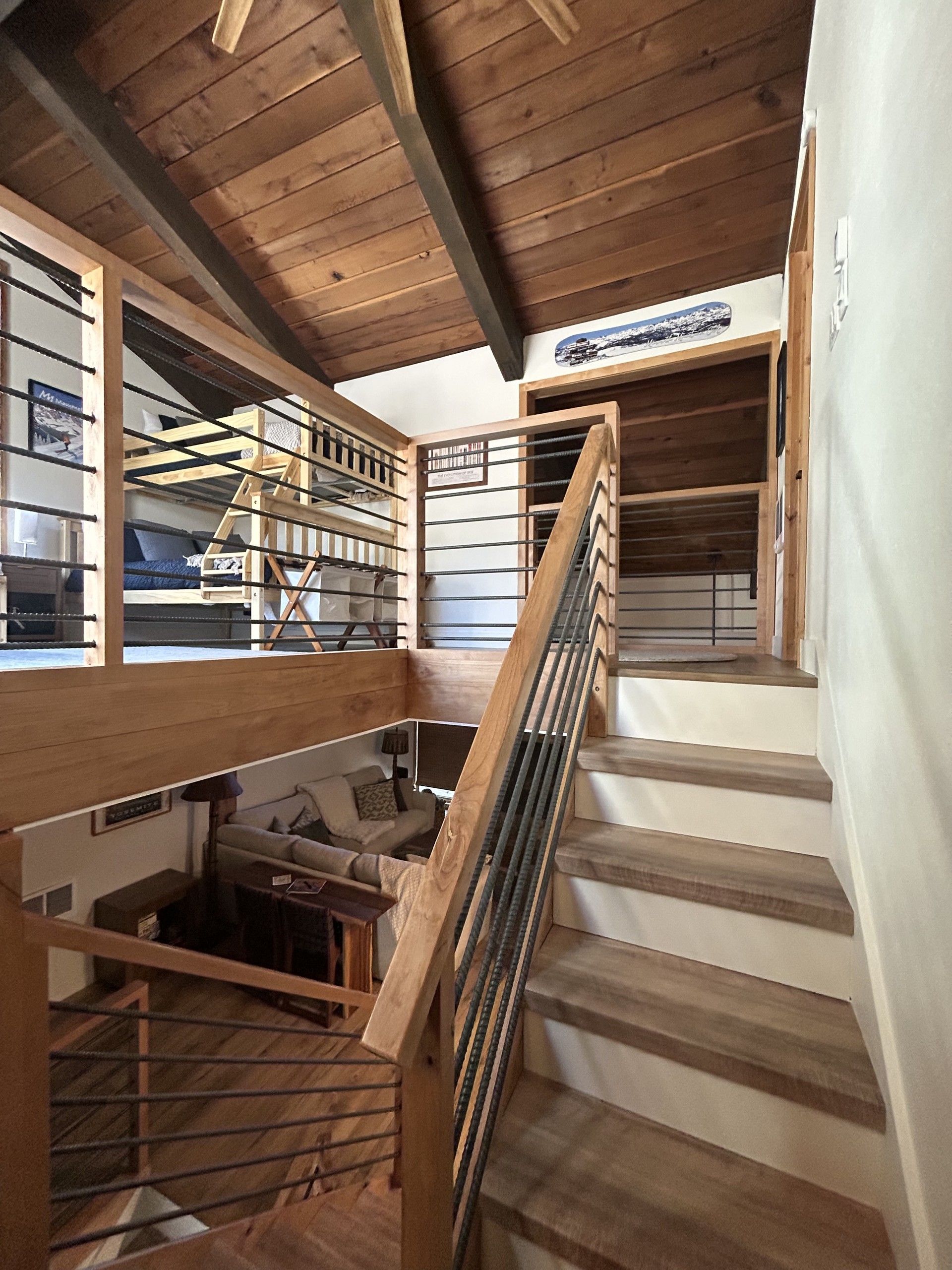 A wooden staircase with a metal railing leading to a loft area with a bunk bed.