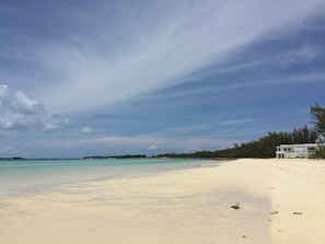 Ein Strand mit einem weißen Gebäude auf der rechten Seite, blauem Himmel und ruhigem türkisblauem Wasser.