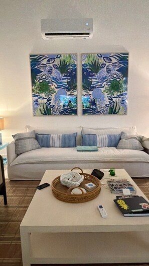 Een woonkamer met een bank, een salontafel met diverse spullen, en twee luchtverkoelingsapparaten aan de muur.