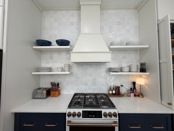 A kitchen with white cabinets, a gas stove, and a range hood. - Brand New Luxury Directly on the Beach | Heated Saltwater Pool | Backup Generator (Governor's Harbour)