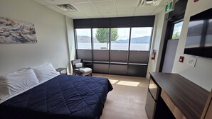 Une chambre d’hôtel comprenant un lit, une chaise, un bureau, une fenêtre donnant sur un lac et un extincteur.