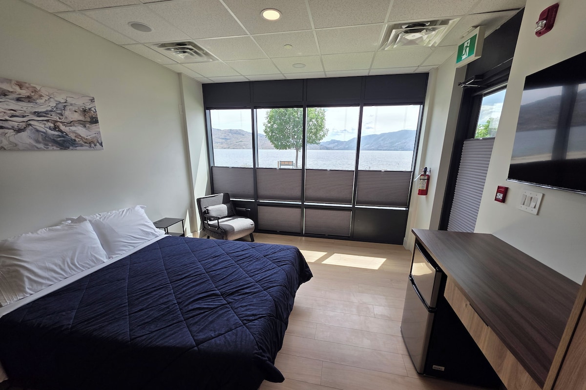 Une chambre d’hôtel comprenant un lit, une chaise, un bureau, une fenêtre donnant sur un lac et un extincteur.