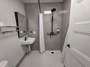 A bathroom with a shower, a sink, a toilet, and a mirror. - Modern Deluxe Loft 103 (Peachland)