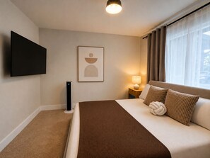 Ein Hotelzimmer mit einem Bett, einem flachbildfernseher an der Wand, einer Nachttischlampe und einem Fenster mit Vorhängen.
