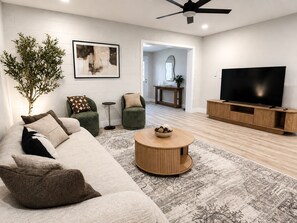 Een moderne woonkamer met een hoekbank, een ronde salontafel, een televisie en een plant.