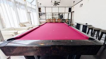A pool table with a red felt surface, a ceiling fan, and a bar area with stools.