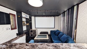 Uma sala de estar moderna com bancada de mármore, um sofá azul, uma mesinha e uma tela de projetor.
