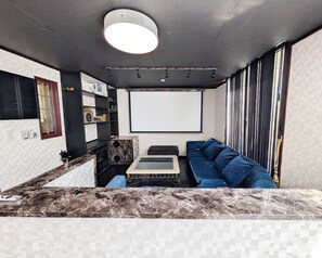Ein modernes Wohnzimmer mit Marmorplatte, einem blauen Sofa, einem kleinen Tisch und einer Projektionsleinwand.
