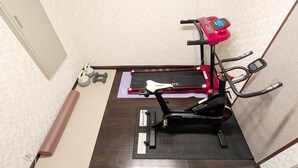 Quarto com bicicleta ergométrica, tapete de yoga e halteres.