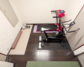Ein Zimmer mit einem Ergometer, einer Yogamatte und einem Hantelpaar.