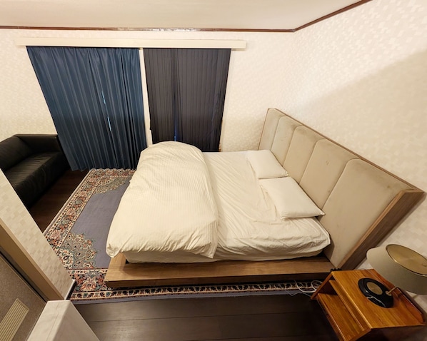 Ein Hotelzimmer mit Bett, Nachttisch, Lampe und einem Fenster mit Vorhängen.