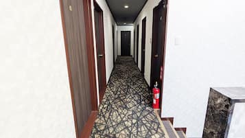A hotel hallway with patterned carpet, wooden doors, and a fire extinguisher.