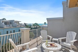 A balcony with white chairs and a table, overlooking a coastal area with buildings and a clear sky. - 30A, Roof Top Views,Walk to Beach, Sleeps 14 (Santa Rosa Beach)