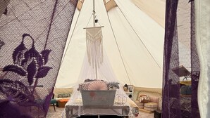 Ein Zelt mit einem Bett, einer Makramee-Hängelampe und einem gemusterten Teppich.