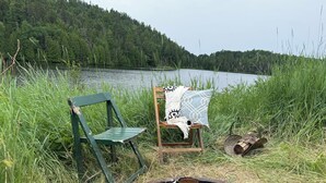 Ein rustikaler Außenbereich mit einer Bank, einem Stuhl, einer Feuerstelle und einem See im Hintergrund.