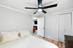 Un dormitorio con una cama, un ventilador de techo, una puerta y un pasillo que conduce a otra habitación.