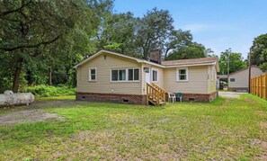 A single-story mobile home with a front porch and a small deck, surrounded by a grassy yard and trees. - Modern 3BR Wilmington Cottage Pet-Friendly • Near Beach & Downtown (Wilmington)