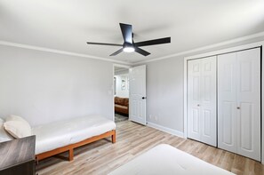 A bedroom with a bed, a ceiling fan, a wardrobe, and a door leading to another room. - Modern 3BR Wilmington Cottage Pet-Friendly • Near Beach & Downtown (Wilmington)