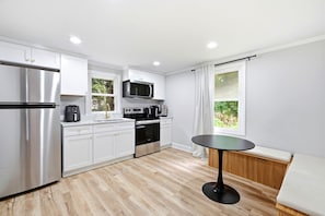 A modern kitchen with stainless steel appliances, white cabinetry, and a dining area with a round table. - Modern 3BR Wilmington Cottage Pet-Friendly • Near Beach & Downtown (Wilmington)