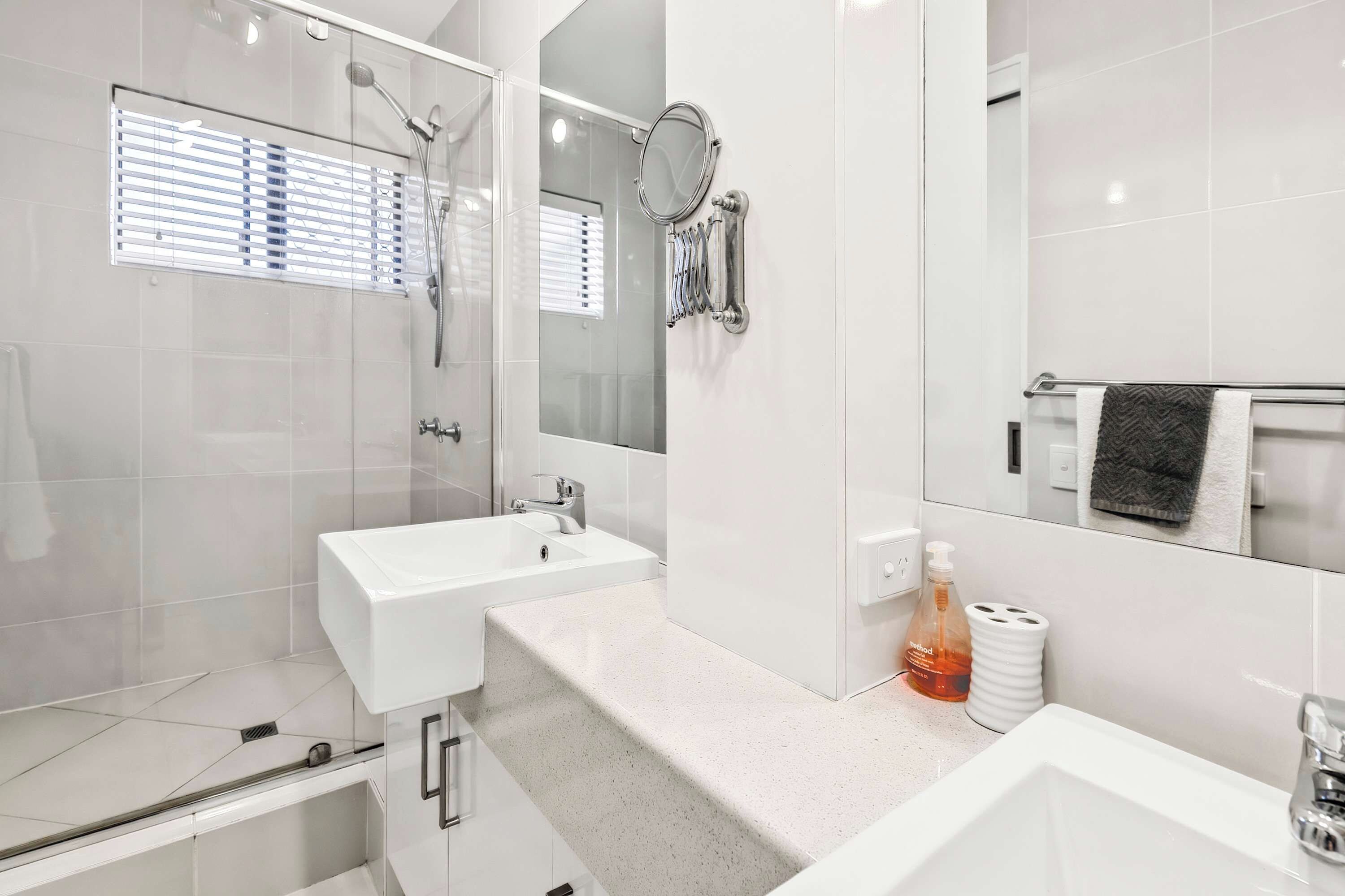 A modern bathroom with a glass-enclosed shower, a white sink, and a large mirror.