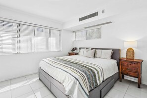 Ein Schlafzimmer mit einem Bett, Nachttischen, einer Lampe und einem Fenster mit Jalousien.