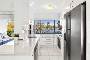 Eine moderne Küche mit einem großen Kühlschrank, weißen Schränken und Blick auf ein Gewässer durch ein Fenster.