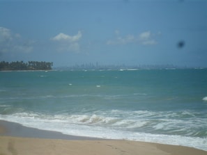 A beach with waves and a distant city skyline.